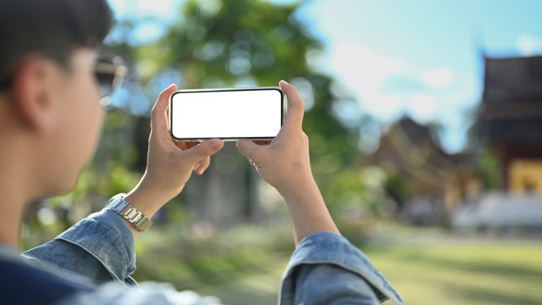 Over shoulder view of asian male tourist taking photo with smart